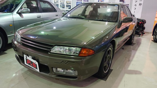 HR32(改)オーテックバージョン<br>1992年4月...スカイラインの父こと櫻井眞一郎氏率いるオーテックジャパンのプロデュースにより、走る歓びを知り尽くした大人のためのグランドツーリングカーがベールを脱いだ。
この上品なイエローイッシュグリーンパールメタリックのボディカラーがひときわ大人のムードを漂わす車両は、GTS-4の4ドアセダンをベースにGT-RのRB26DETT からターボを取り去り、
220psを発揮するRB26DEを移植した他、それに伴う高い制動性能、快適な乗り心地のためのサスペンションを採用するなどし、“街乗りからスポーツ走行まで“を安全に且つ高質な走りにすることをコンセプトに生まれてきた。それは「GT-Rに興味はあるけれど4ドアがいい」「ハイパワーよりもフィーリングが大事」など、スカイラインにこだわりを持つユーザーに奉げられた限定198台のスペシャルカーである。
